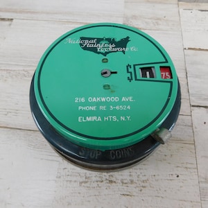 May include: A round, green and dark gray metal coin bank with a mechanical counter showing 75. The top features the text National Stainless Cookware Co., 216 Oakwood Ave., Phone RE 3-6524, Elmira Hts, N.Y. The side base is embossed with STOP COINS.