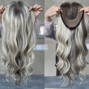 May include: A blonde human hair topper with a wavy texture. The topper is shown on a mannequin head with the base of the topper visible.