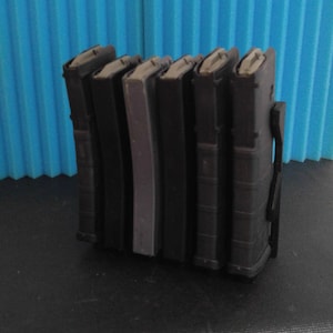 May include: A close-up of six black magazine holders for firearms. The holders are stacked vertically and have a textured surface.