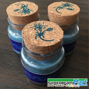 Può includere: Tre barattoli di vetro con liquido blu e tappi di sughero. Ogni tappo ha un disegno floreale blu. I barattoli sono etichettati con "SUPER FAMIMart".