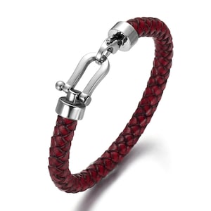 May include: A red braided leather bracelet with a silver clasp. The clasp is a U-shaped hook with a small ball on the top.