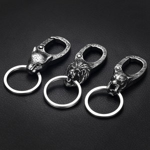 May include: Three silver keychains with animal head designs. The keychains feature a wolf, a lion, and a tiger head. Each keychain has a silver ring and a silver hook.