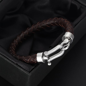May include: A brown leather bracelet with a silver clasp. The bracelet is braided and has a polished metal finish.