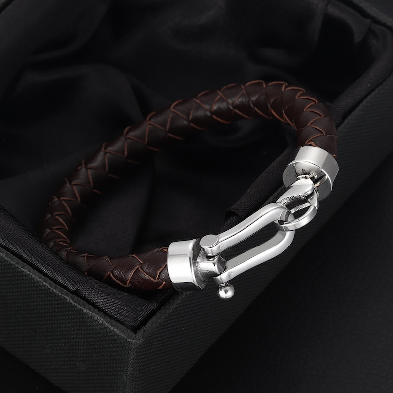 May include: A brown leather bracelet with a silver clasp. The bracelet is braided and has a polished metal finish.