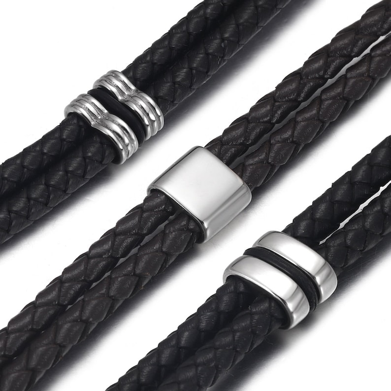 May include: Two black leather bracelets with silver metal accents. The bracelets are braided and have a simple design.