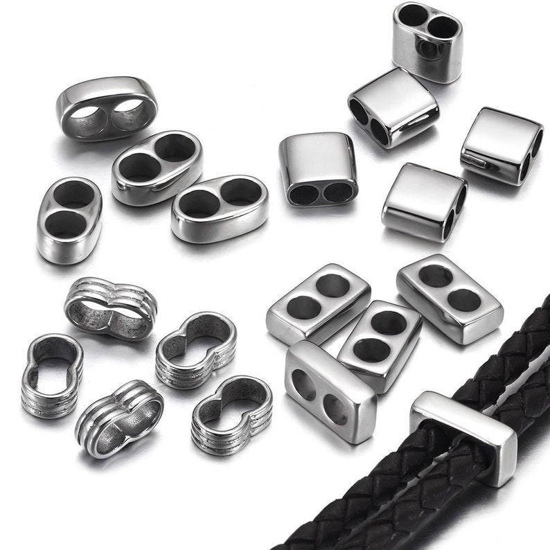 May include: A set of silver-toned metal jewelry findings, including oval and rectangular shapes with double holes, and decorative links with a braided design. The findings are shown on a black leather cord.