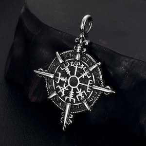 May include: A silver-colored pendant featuring a Viking compass design, also known as Vegvísir. The pendant has a circular center with runic symbols and eight pointed arms. The pendant is suspended from a small loop.