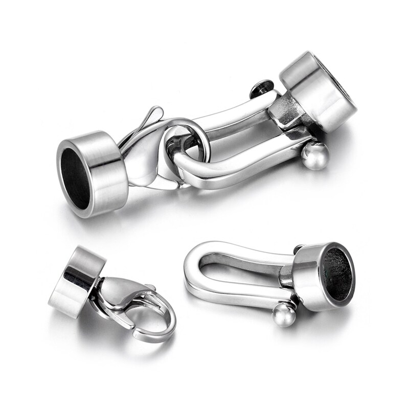 May include: Silver-toned metal clasp with a hook and loop closure. The clasp has a cylindrical end cap on each side.