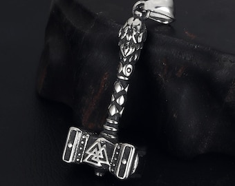 May include: A silver pendant shaped like Thor's hammer, Mjolnir. The hammer has detailed patterns on the head and handle, with a loop for a chain. The design includes a triangle symbol and decorative elements.