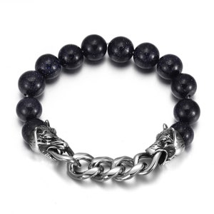May include: A black beaded bracelet with wolf head clasps. The beads are made of black stone with a speckled texture. The clasps are made of silver metal and feature detailed wolf heads.
