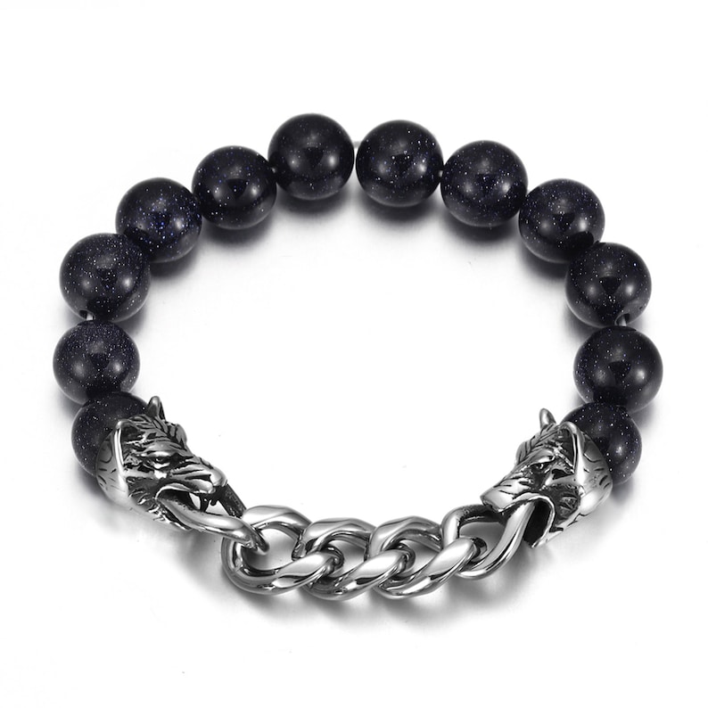 May include: A black beaded bracelet with wolf head clasps. The beads are made of black stone with a speckled texture. The clasps are made of silver metal and feature detailed wolf heads.