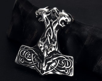May include: A silver-coloured pendant shaped like Thor's hammer, Mjolnir. The hammer has detailed knotwork and two animal heads at the top. The pendant is made of a shiny metal and is set against a dark background.
