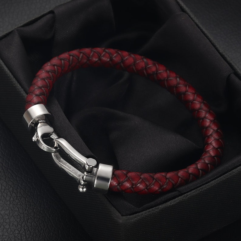 May include: A braided leather bracelet with a silver clasp. The bracelet is a dark red color.