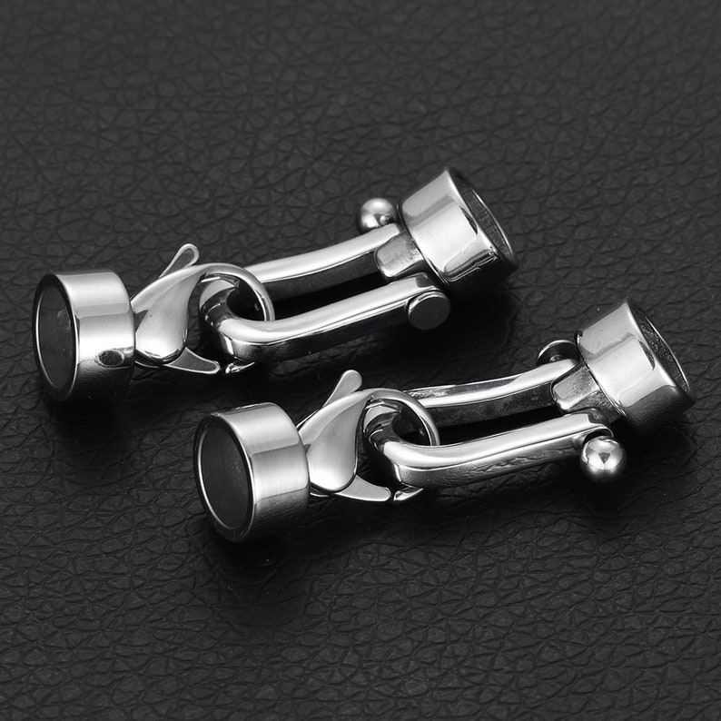 May include: Two silver metal clasps with a hook and loop closure. The clasps are designed to connect two pieces of jewelry or other items.