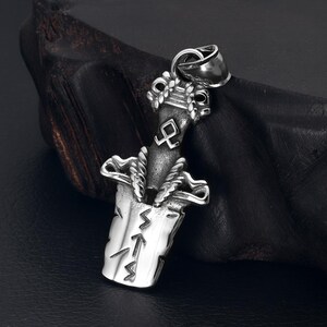 May include: A silver pendant in the shape of a sword with a rope-like design around the hilt. The blade of the sword has a symbol on it and the handle has a knot-like design. The pendant is hanging from a chain.