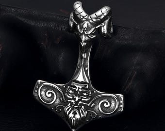 May include: A silver pendant shaped like Thor's hammer, with a ram's head and detailed face on the hammerhead. The design includes intricate scrollwork and a textured finish. The pendant is a symbol of Norse mythology.