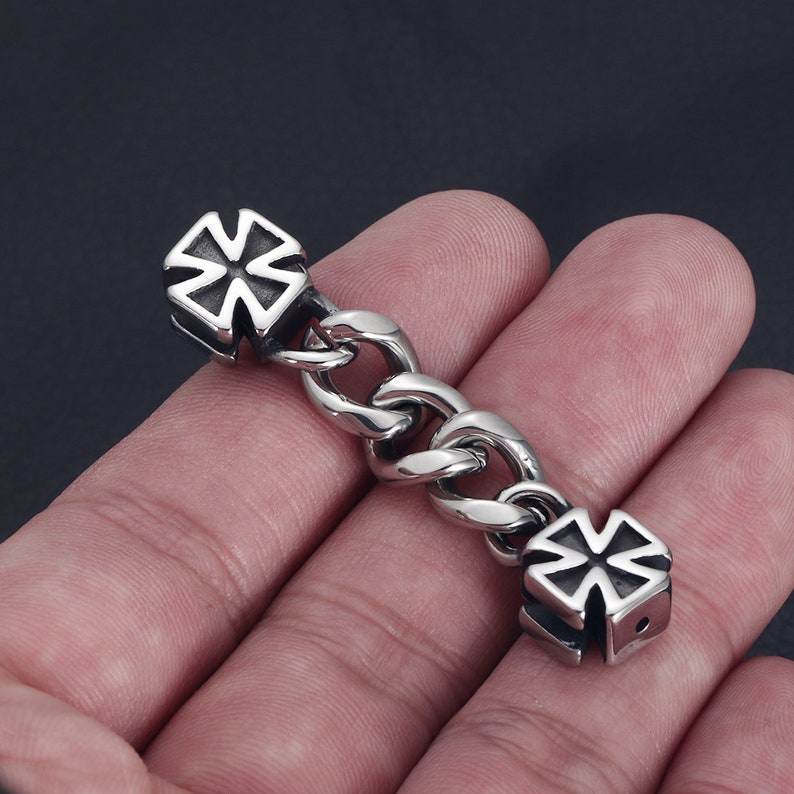 May include: A silver chain bracelet with two silver cross-shaped charms. The bracelet is made of a thick, curb chain.