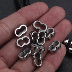 May include: A close-up of a pile of silver metal beads with a double-loop design. The beads are smooth and shiny.