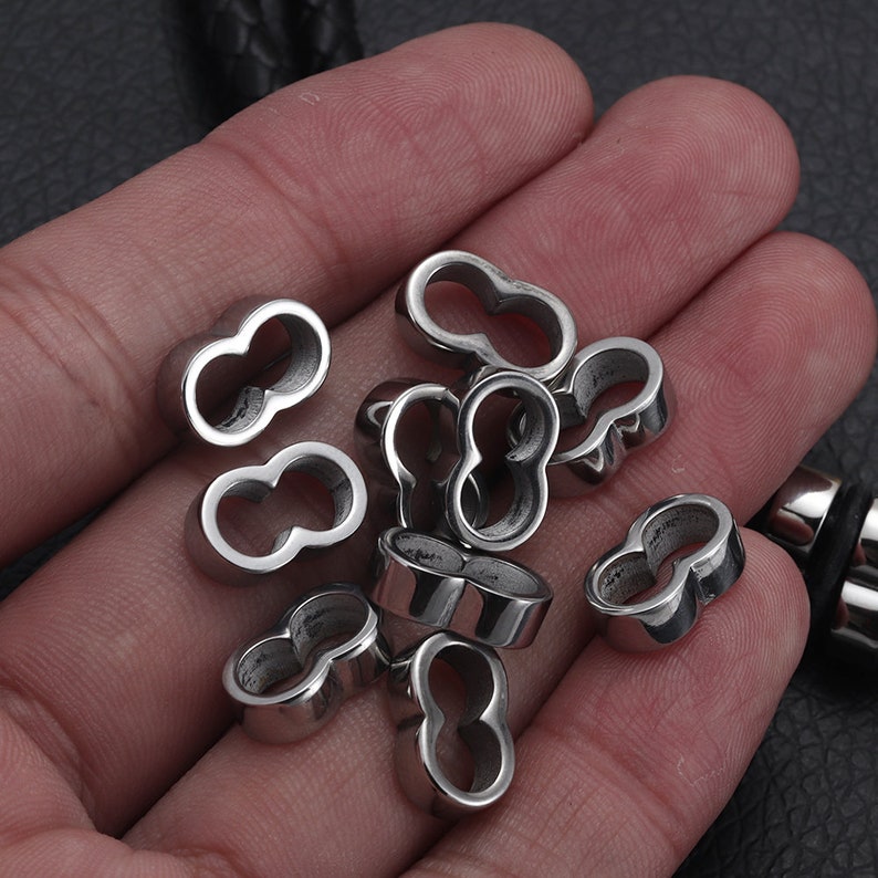 May include: A close-up of a pile of silver metal beads with a double-loop design. The beads are smooth and shiny.