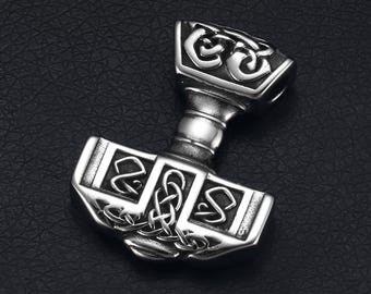 May include: A silver-coloured pendant shaped like Thor's hammer, Mjolnir. The hammer has detailed Celtic knotwork and geometric designs on the head and handle. The pendant is shown against a dark background.