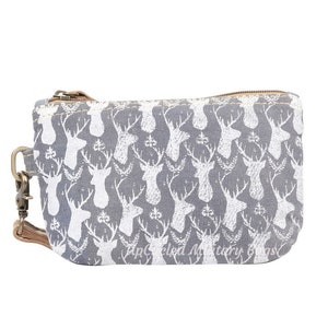 May include: A gray canvas zippered pouch with a white deer print pattern. The pouch has a brown leather strap with a metal clasp.