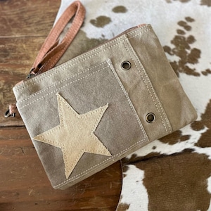 May include: A brown canvas zippered pouch with a large beige star applique. The pouch has a brown leather strap and two metal grommets.