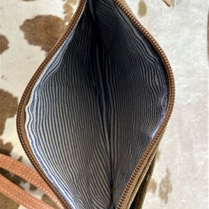 May include: A brown leather zippered pouch with a white and blue striped lining. The pouch has a long strap.