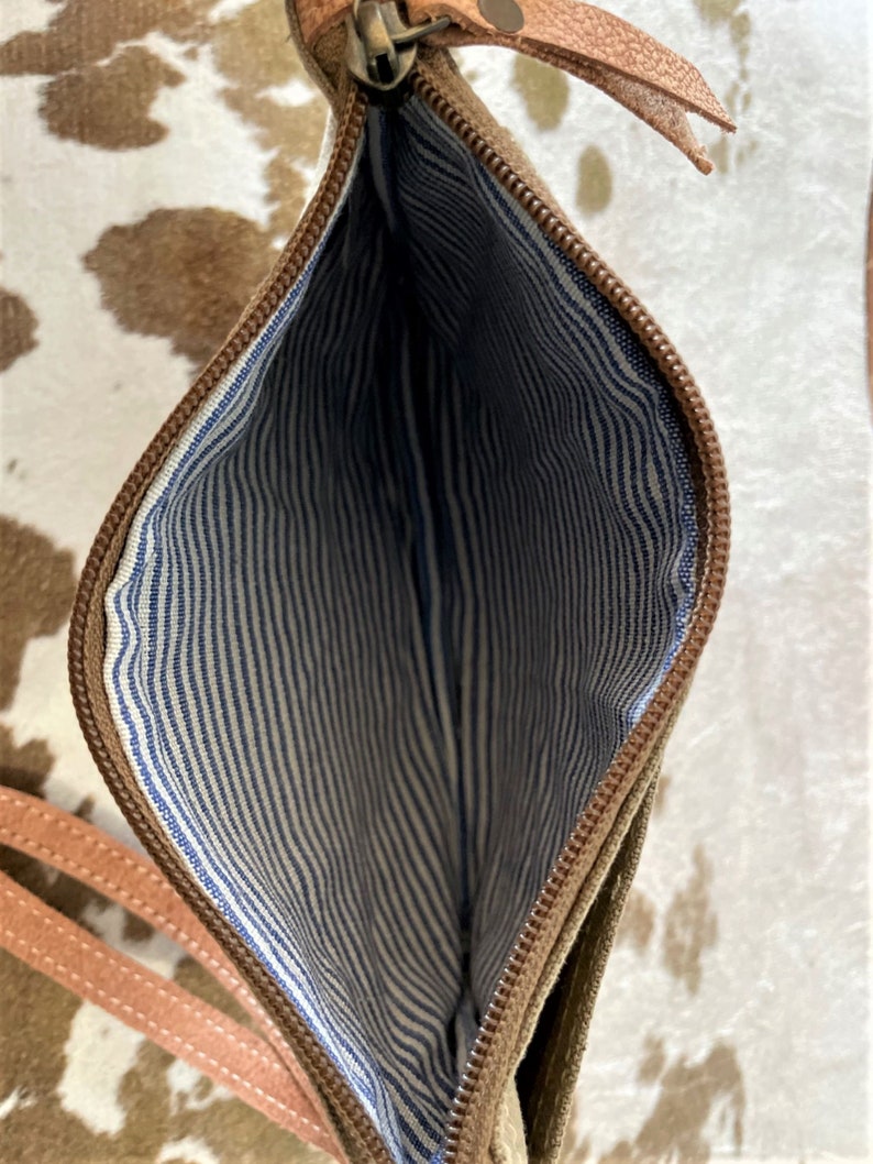 May include: A brown leather zippered pouch with a white and blue striped lining. The pouch has a long strap.