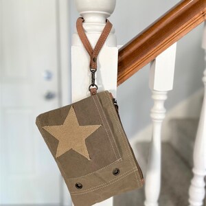 May include: A small, green canvas bag with a large tan star on the front. The bag has a brown leather strap and a zipper closure.