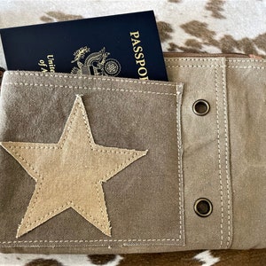 May include: A brown canvas travel pouch with a large beige star on the front. The pouch has a zipper closure and two metal eyelets on the side. A passport is visible inside the pouch.