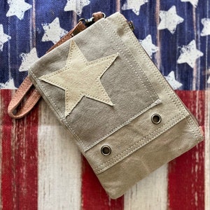 May include: A gray canvas zippered pouch with a large white star on the front. The pouch has two metal eyelets on the bottom and a brown leather strap.