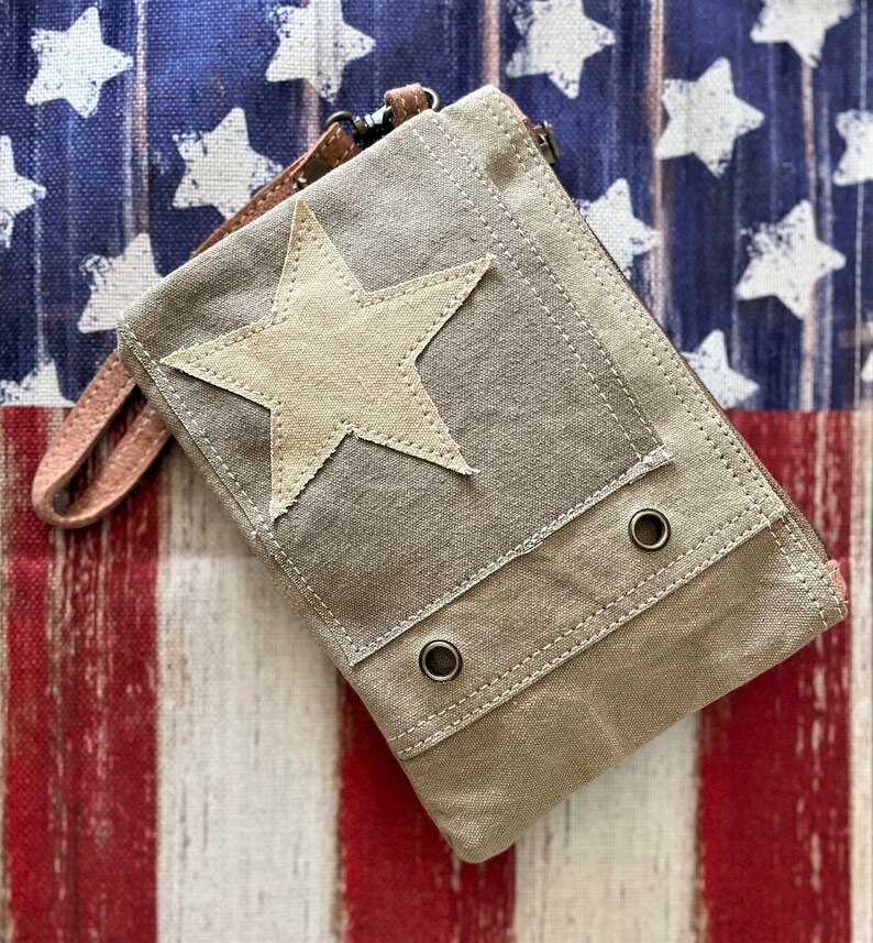 May include: A gray canvas zippered pouch with a large white star on the front. The pouch has two metal eyelets on the bottom and a brown leather strap.