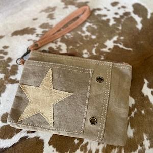 May include: A small, brown canvas clutch with a zipper closure and a star-shaped patch. The clutch has a brown leather strap and two metal eyelets on the front.