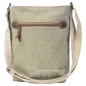 May include: A light green canvas crossbody bag with a zippered pocket and a brown leather strap. The bag has a white strap and the text "RecycledMilitaryBags.com" is printed on the bottom.