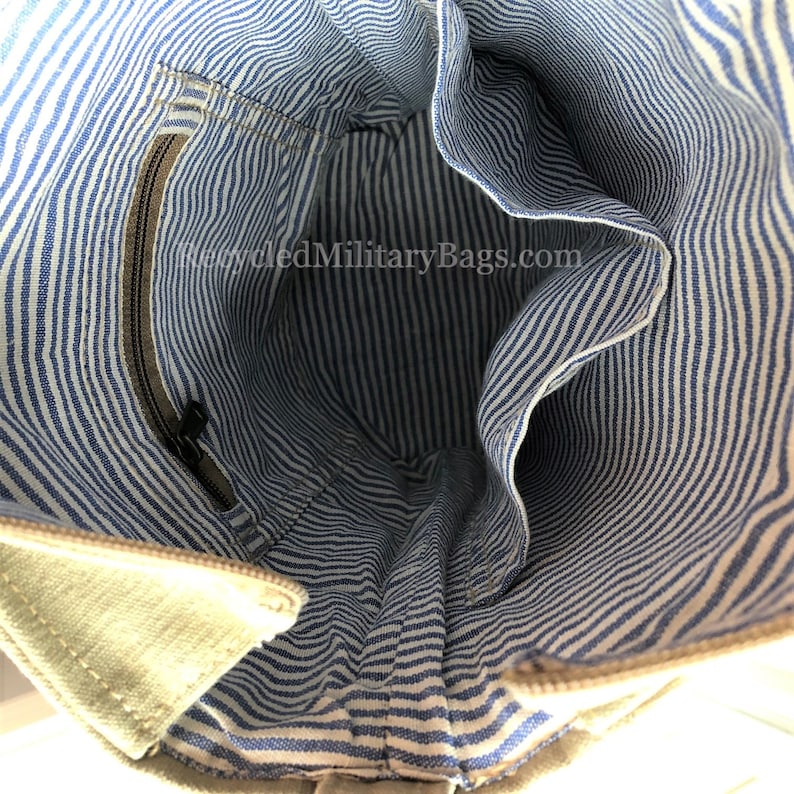 May include: The inside of a beige canvas tote bag with a blue and white striped lining. The bag has a zippered pocket on the inside.