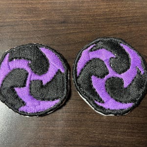 May include: Two purple and black embroidered patches with a three-pointed star design.