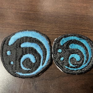 May include: Two embroidered patches with a blue and black swirling design. The patches are circular and have a white backing.