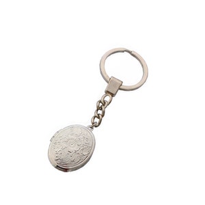 Puede incluir: Llavero de plata con forma de medall&oacute;n ovalado con un dise&ntilde;o floral. El llavero tiene una cadena de plata y un anillo de plata.