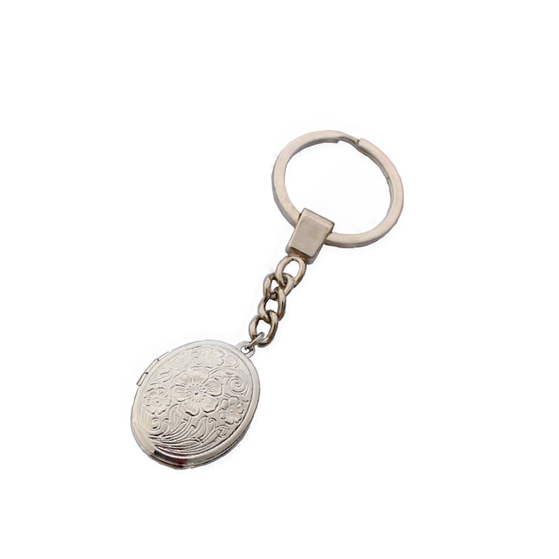 Puede incluir: Llavero de plata con forma de medall&oacute;n ovalado con un dise&ntilde;o floral. El llavero tiene una cadena de plata y un anillo de plata.