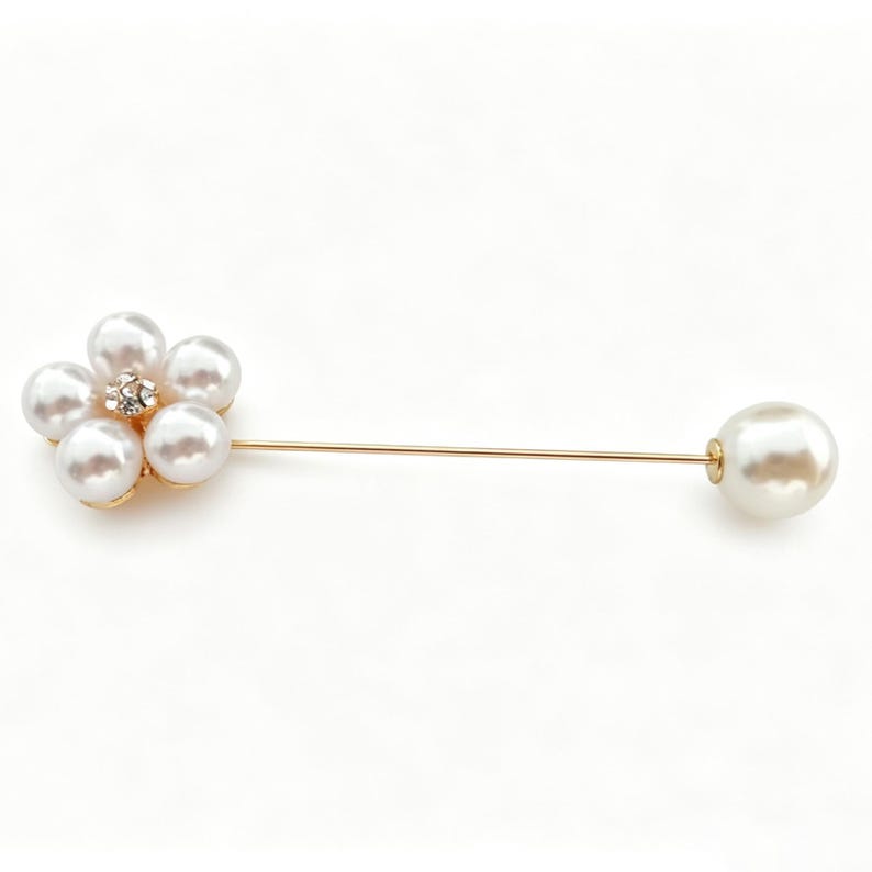 May include: A gold-toned lapel pin featuring a flower-shaped cluster of five white faux pearls with a small clear rhinestone at the center. The pin has a long, thin gold-toned metal stem that ends with a single, larger white faux pearl at the tip.