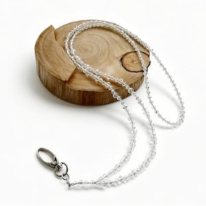 May include: A lanyard made of small, clear, faceted beads strung together in a continuous loop. The lanyard features a silver-toned metal lobster claw clasp at the bottom, designed for attaching items such as identification badges or keys.