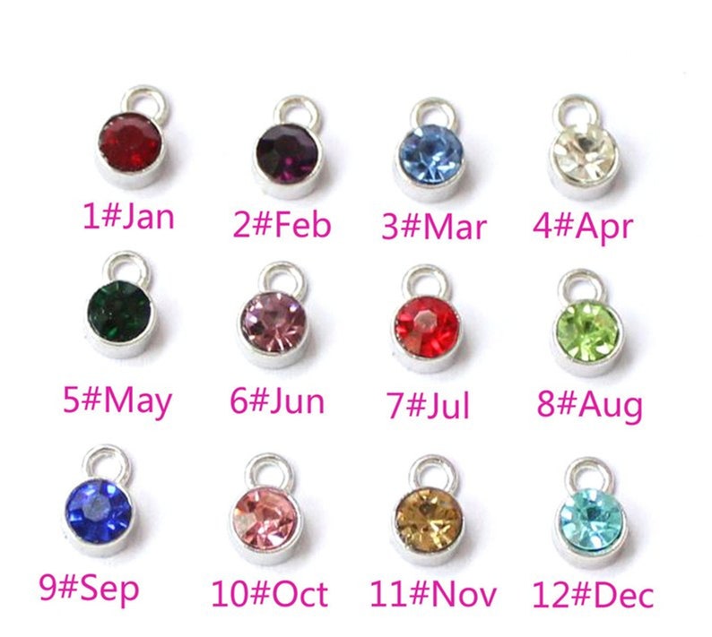 May include: A collection of twelve silver-toned charms, each with a different colored gemstone. Each charm is labeled with a month of the year, from January to December. The gemstones are various colors, including red, purple, blue, and green.