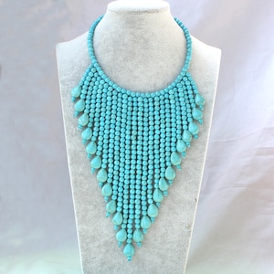 May include: A turquoise blue statement necklace with a cascading design of round beads and teardrop-shaped beads.