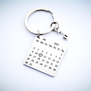 May include: Silver keychain with a calendar charm. The calendar is for January 2022 with a heart on the 11th.