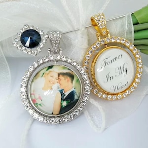 May include: Two photo pendants with clear crystal accents. One pendant has a photo of a couple, the other has the text "Forever In My Heart". A blue crystal earring is also visible. The pendants are on a white ribbon.
