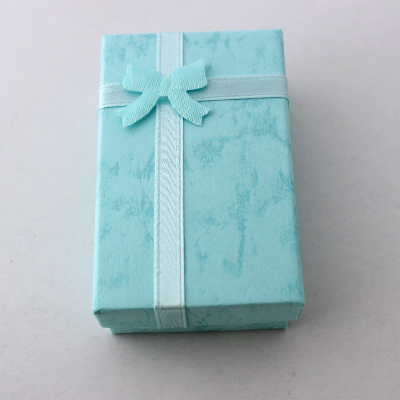 May include: A rectangular, light blue gift box with a textured surface. A light blue ribbon with a bow is wrapped around the box. The box is closed and ready for gifting.