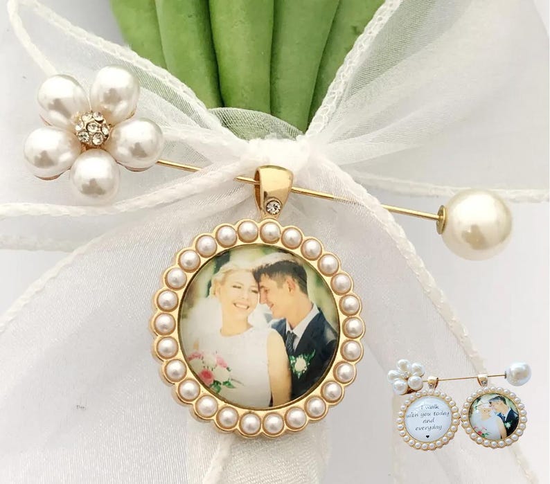 May include: A gold-toned brooch featuring a circular frame bordered by small white pearls, enclosing a photograph of a couple. The brooch is attached to a white ribbon and includes a flower-shaped accent with pearls and clear crystals.