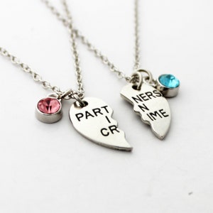 May include: Two silver necklaces with heart-shaped pendants, each split in half. One pendant reads "PART I CR" and has a pink gemstone. The other reads "NERS N IME" and has a blue gemstone. The necklaces are connected by delicate chains.