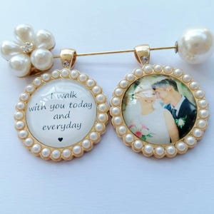 May include: A gold-toned brooch featuring two circular pendants framed by small white faux pearls. One pendant displays the text I walk with you today and everyday with a small heart. The other pendant shows a photograph of a couple. A large faux pearl sits at one end of the pin.