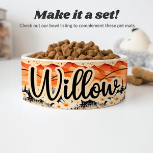 May include: White ceramic pet bowl with a colorful mountain and flower design. The bowl has the name "Willow" written on it in black cursive lettering.